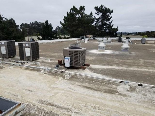 Weathered light commercial roof with multiple gray HVAC units, mushroom vents, and white conduits under an overcast sky.
