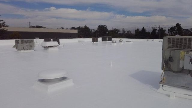 Bright white newly coated commercial roof with HVAC units and vents under a clear blue sky.