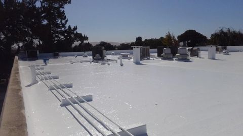 High view of a fully white reflective coated commercial roof with HVAC equipment and trees along the perimeter.