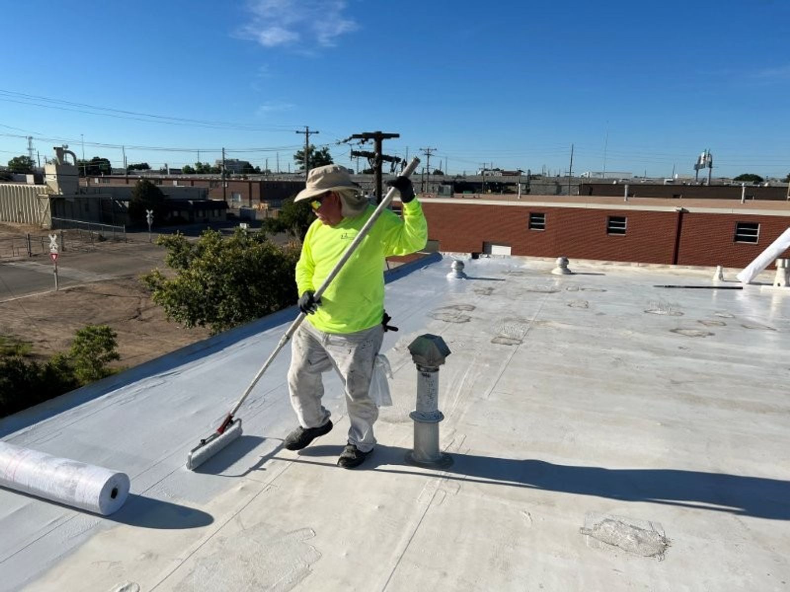Workers installing overlay materials on a flat commercial roof under bright sun.