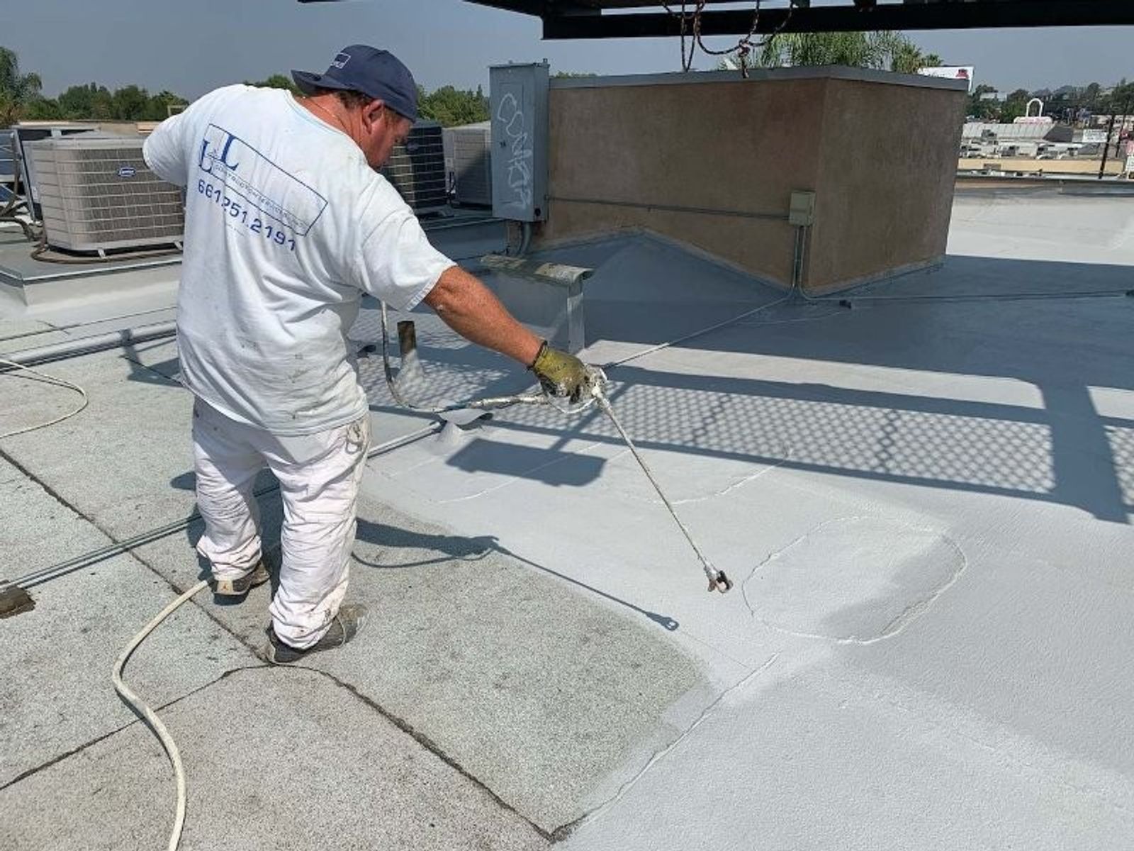 Wide view of a flat commercial roof with solar racking and workers applying coating materials.
