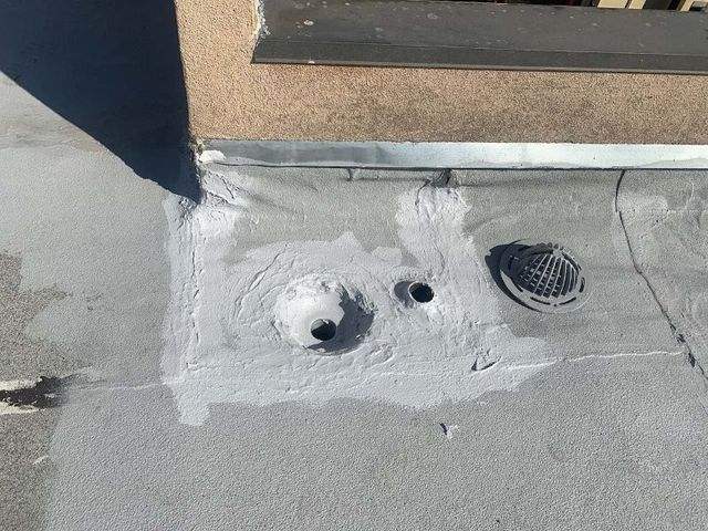 Close-up of a flat roof drain and nearby pipe sealed with fresh gray mastic, drain grate resting beside the bowl.