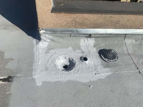 Close-up of a flat roof drain and nearby pipe sealed with fresh gray mastic, drain grate resting beside the bowl.