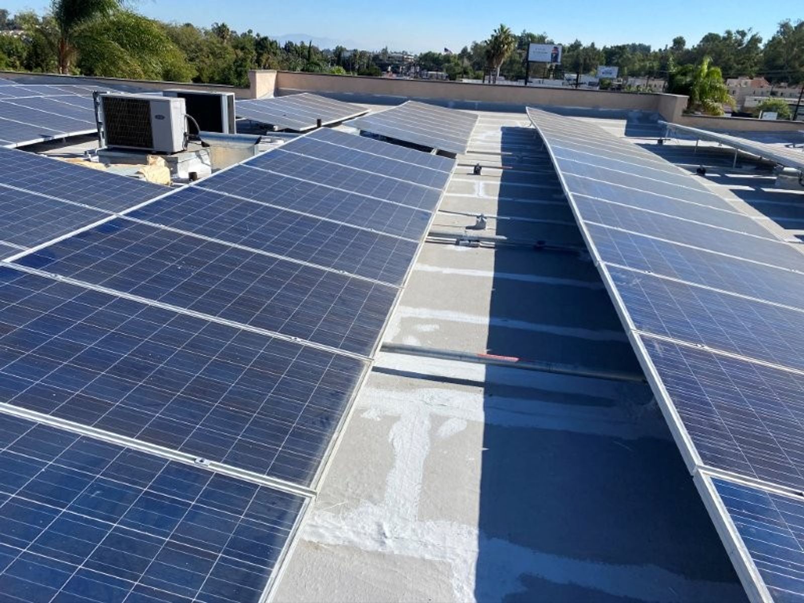 Finished bright white coated commercial roof with solar panel arrays and HVAC equipment under a clear sky.