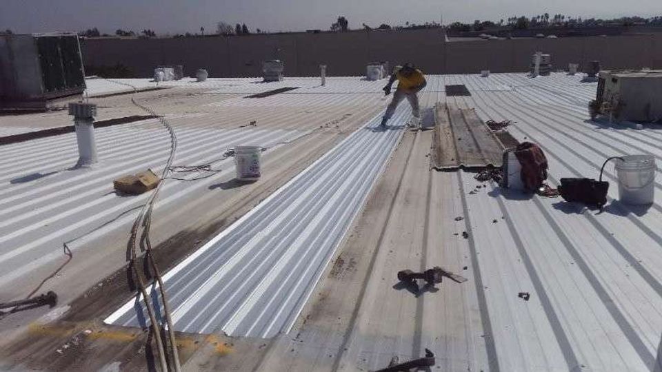 Worker installing new bright white corrugated metal roof panels next to weathered tan metal panels and HVAC units.