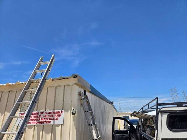 Metal roof repair in progress on a commercial building with corrugated panels and rooftop equipment.