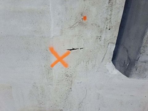 Weathered roof surface marked with orange spray paint next to a small crack.