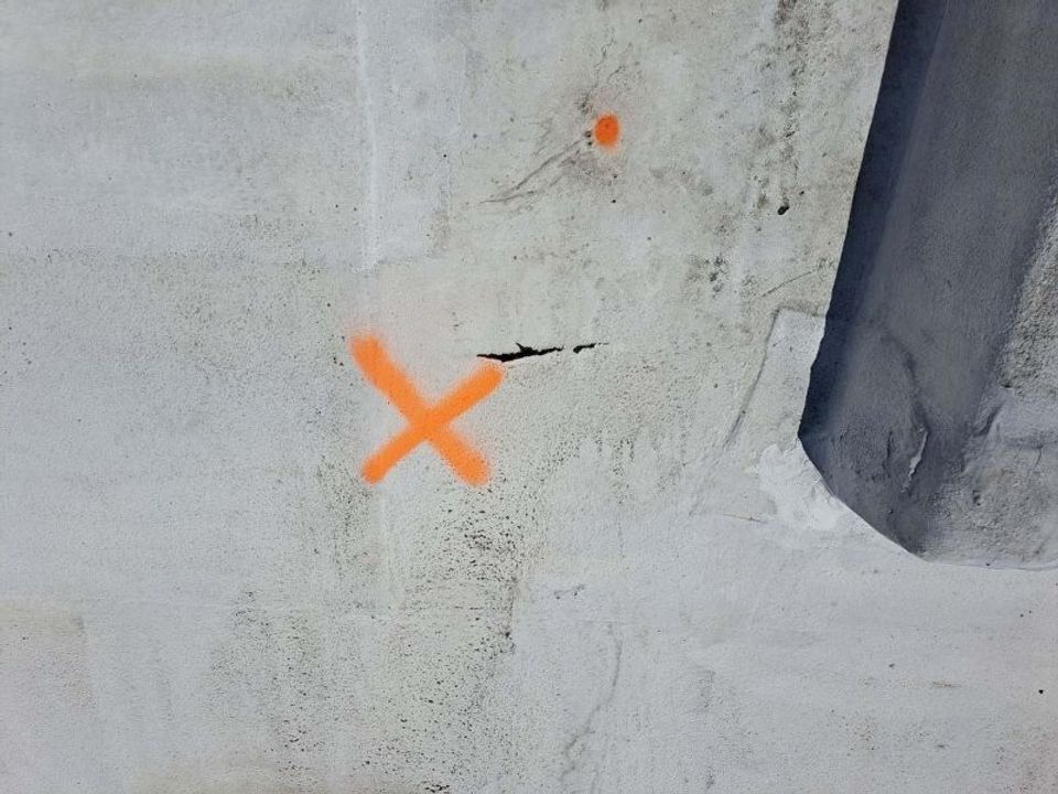 Weathered roof surface marked with orange spray paint next to a small crack.