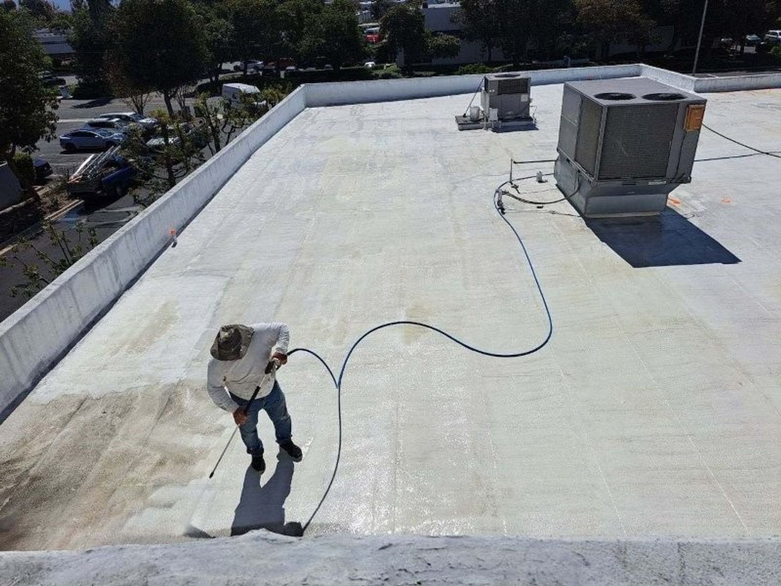 Wide shot of a cleaned commercial roof field with HVAC curbs and parapet walls under a clear sky.